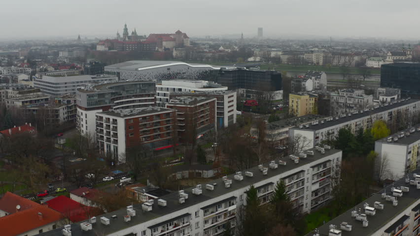 Aerial view of foggy Krakow, eastern residential apartment blocks in the foreground, historic city center with Wawel Castle far in the background, autumn - tilt up, crane up shot.