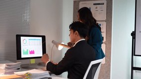Two young asian businesspeople analyzing financial data graphs on a desktop computer while working overtime in a modern office, discussing company growth and brainstorming new marketing strategies - Powered by Shutterstock - Get 15% off with code: PIKWIZARD15