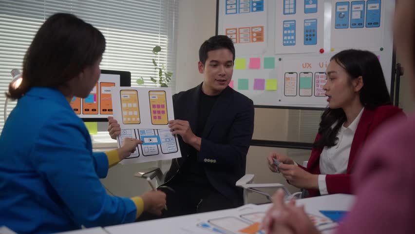 Young Asian business professionals meeting to plan a mobile application. UI UX developers working on a smartphone screen project together