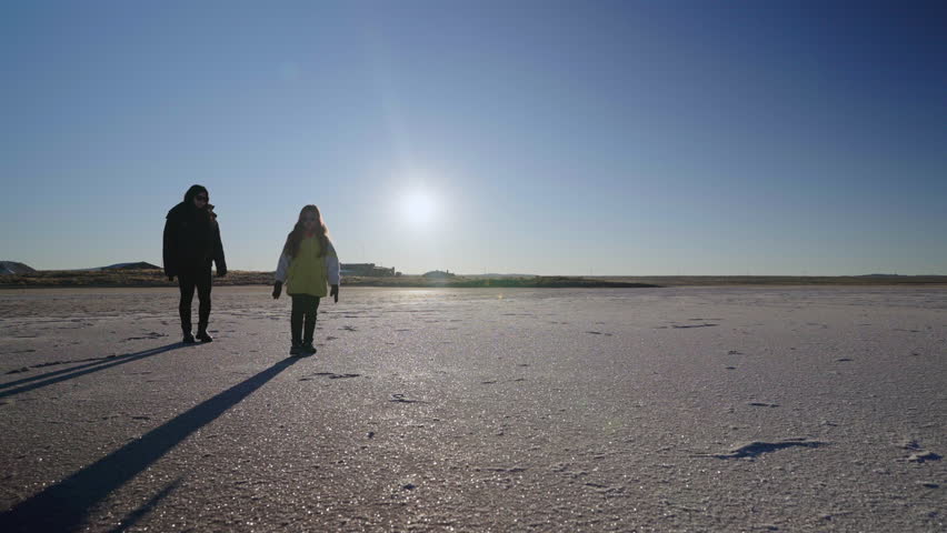 Mother and daughter walking across desert and frozen salt flat, lake during cold winter sunset.