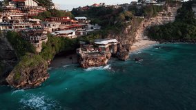 Cinematic drone footage showcasing Bali cliffside restaurants above a calm turquoise cove with shallow reef water, gentle waves and warm golden hour light along the tropical coastline - Powered by Shutterstock - Get 15% off with code: PIKWIZARD15