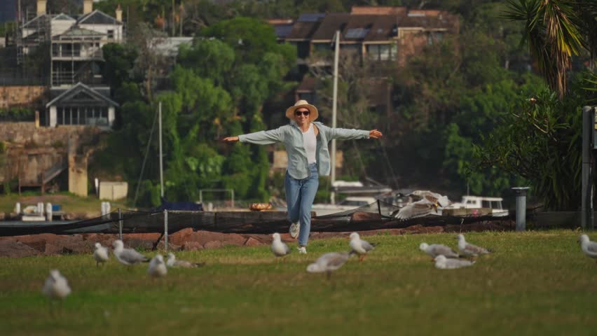 Tourist Interacts With Seagulls At Harbor, Woman In Straw Hat Feeds Seagulls Overlooking Marina