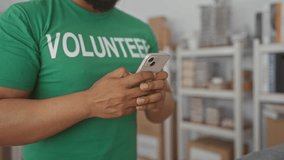 Man wearing green volunteer shirt texting on smartphone with hands in donation center building; community service compassion. - Powered by Shutterstock - Get 15% off with code: PIKWIZARD15