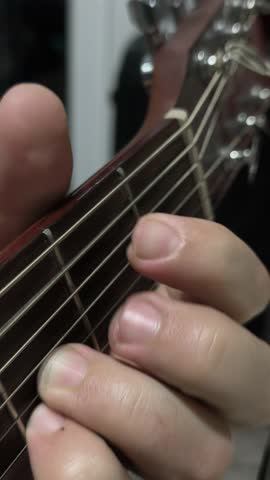 vertical video. Close view of hands playing acoustic guitar indoors. Warm light and wooden texture emphasize calm musical moment. Musician strumming guitar strings in soft evening light.