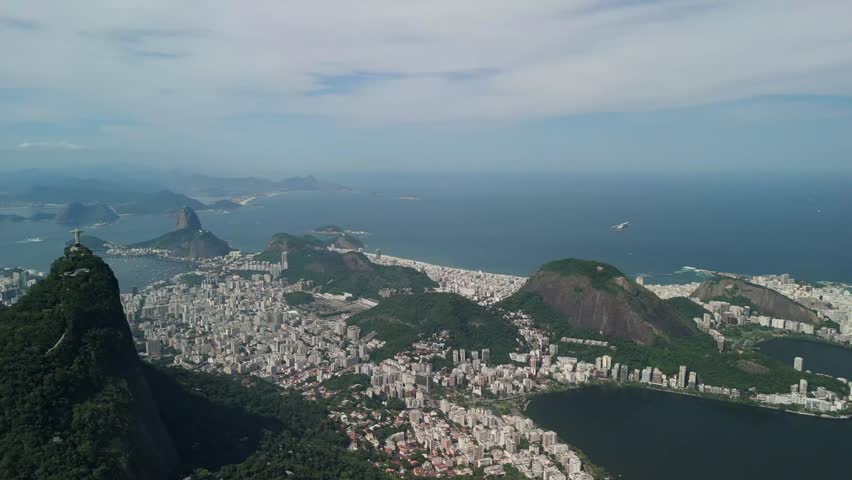 Aerial slow pan left follows a helicopter flying past Christ the Redeemer above the urban landscape of Rio de Janeiro