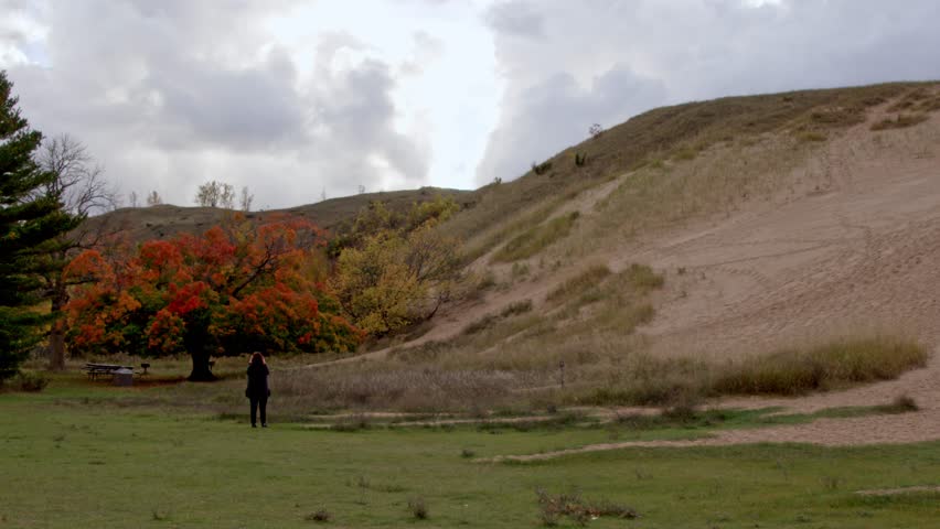 Middle aged woman taking photos of the Dune Climb at the Sleeping Bear Dunes National Lakeshore in Michigan on a cloudy autumn day with stable video.