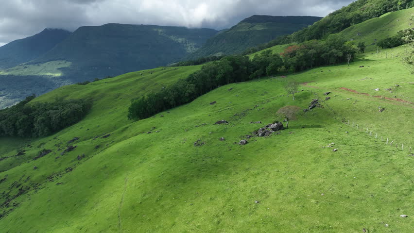 Dramatic 4K drone shot rising and panning right to reveal an imposing rocky mountain covered in lush vegetation at Tajuvas Canyon, Morrinhos do Sul, Brazil. Majestic nature landscape.
