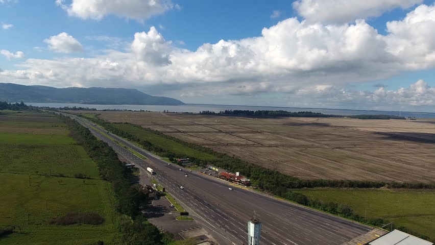 Cinematic 4K drone shot pulling back diagonally to reveal a busy highway toll plaza on BR-290 freeway with trucks and cars in Rio Grande do Sul, Brazil. Sunny day landscape.