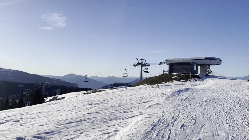 Panoramic View of Top Station of Ski Chairlift with Skiers Getting Off and Stunning Alpine Mountain Range Horizon on Sunny Winter Day Ideal for Travel Commercials and Winter Holiday Concepts in Europe
