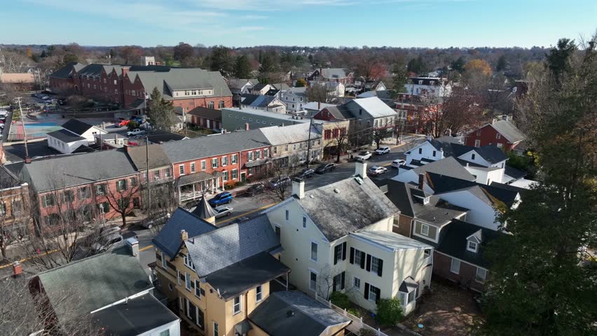 Aerial approaching shot of historic Lititz city, Pennsylvania in winter, showing small-town streets, brick buildings and residential houses with light snow under clear seasonal sky. Wide shot.