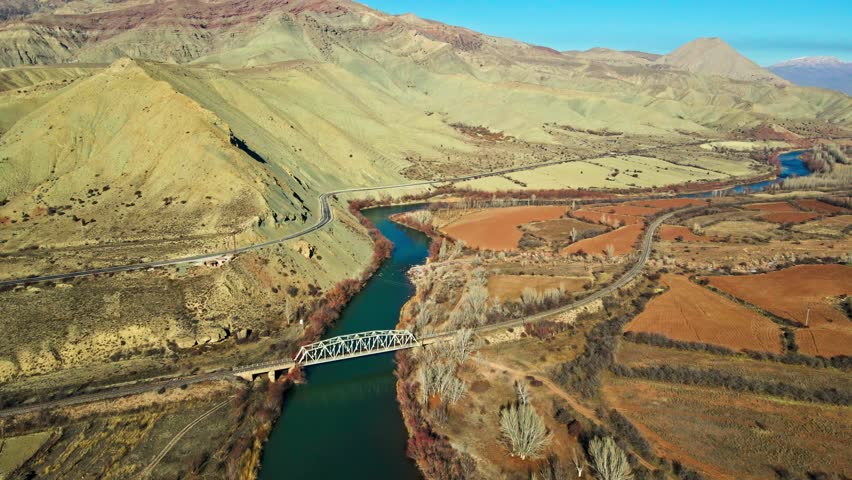 A green and brown landscape with a river running through it. The river is surrounded by hills and trees