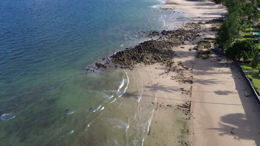Aerial drone footage of Long Beach on Koh Lanta featuring turquoise water, sandy shoreline and a distinctive coastal pine forest, creating a calm tropical island landscape without people.