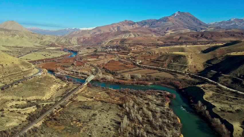 A beautiful landscape with a river running through it. The sky is clear and the sun is shining brightly