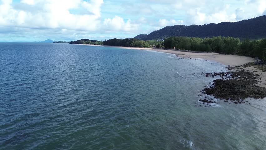Aerial drone footage of Long Beach on Koh Lanta featuring turquoise water, sandy shoreline and a distinctive coastal pine forest, creating a calm tropical island landscape without people.