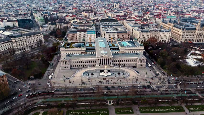 Aerial drone shot panning left over the Austrian Parliament Building, revealing Vienna’s cityscape of historic rooftops, broad avenues, and light traffic, captured in clear winter sunlight