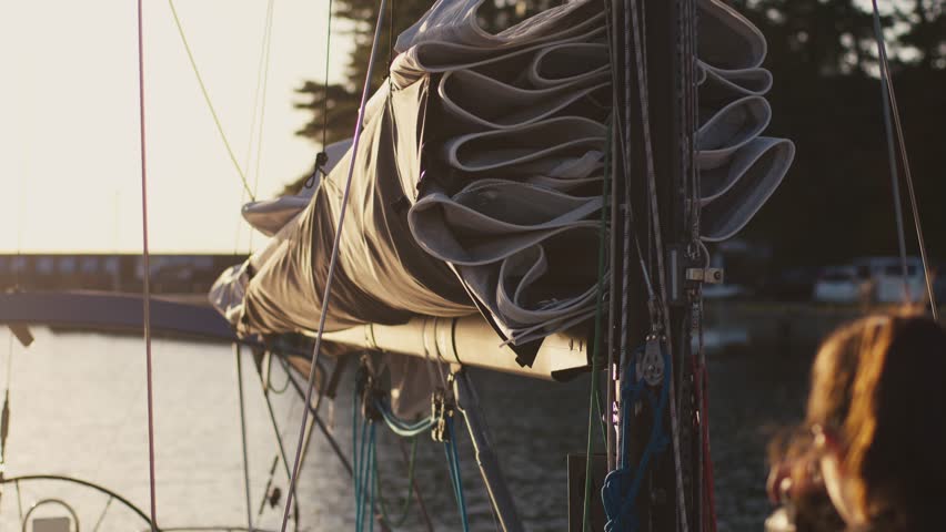 Silhouette Of Sailor Handling Mooring Lines On Yacht At Sunset, Golden Hour Backlight Over Calm Harbor Water