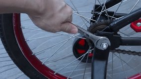 close up of left hand using a wrench to loosen a nut and remove bicycle rear wheel , showing chain, spokes, and axle detail during bike repair and maintenance work for kid playing in park on holiday - Powered by Shutterstock - Get 15% off with code: PIKWIZARD15