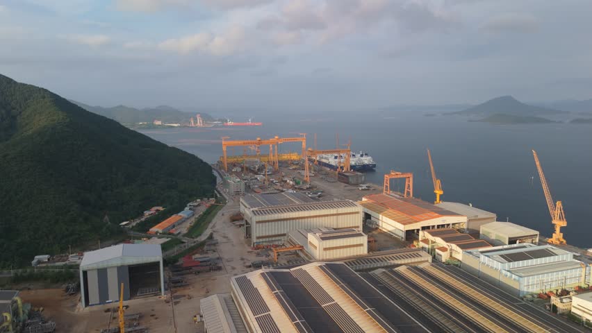 Panoramic aerial view of a vibrant shipyard with colossal gantry cranes, ships under construction, and industrial facilities, some featuring solar panels.