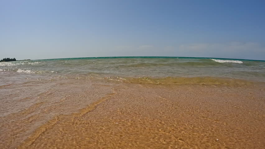 Big Waves Splash onto the Sandy Shore of Lake Michigan. Big beautiful waves of crystal clear water crash onto the beach of Lake Michigan. Water is turquoise colored with views to the sand below. Unspoiled nature located within Wilderness State Park in Northern Michigan, USA.