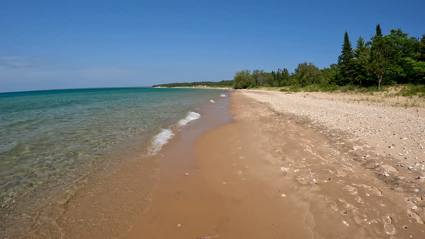 Stunning Natural Beauty on the Sandy Shore of Lake Michigan. Moving downwards as the waves roll in on the sandy shores of Lake Michigan. Pristine, untouched natural beauty. Sand dunes and forest line the beach. Unspoiled nature located within Wilderness State Park in Northern Michigan, USA.