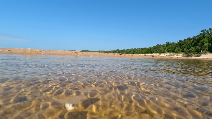 Ripples of Water on the Sandy Beach of Lake Michigan. Surface level views of a shallow inlet of water on the beaches of Lake Michigan. The water is transparent with views of the sand and rocks below. Unspoiled nature located within Wilderness State Park in Northern Michigan, USA.