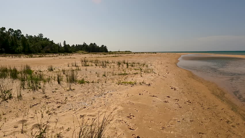 Beautiful Wilderness Beach on Lake Michigan. Beautiful untouched natural beach beauty on the shores of Lake Michigan. A small inlet of water ripples atop the sandy beach with wild grasses. Located within Wilderness State Park in Northern Michigan, USA.