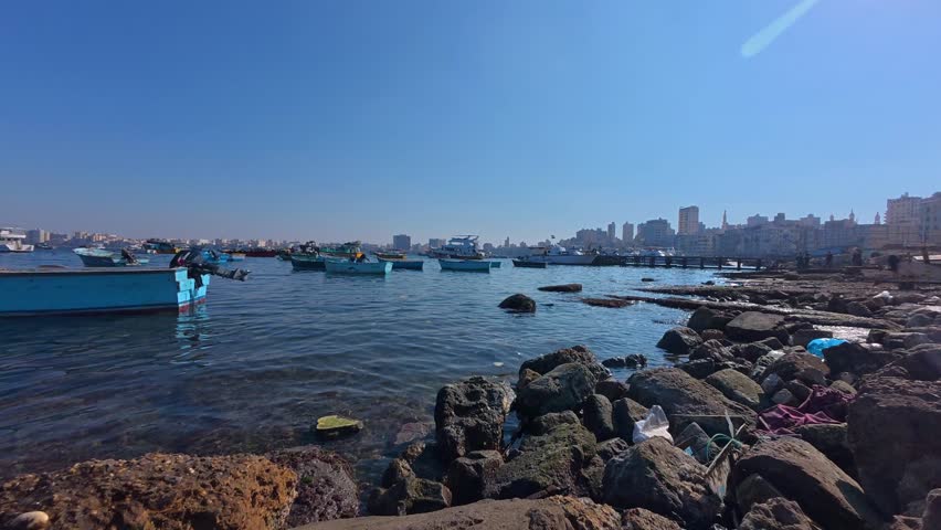 Wide-angle time-lapse footage showing small fishing boats floating at calm Mediterranean sea in the harbor of Alexandria under a clear blue sky