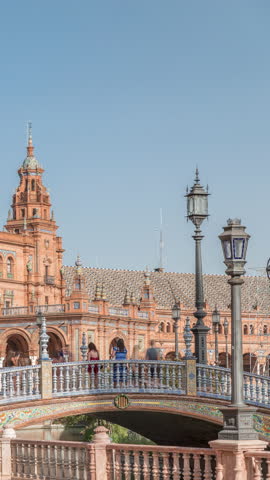 Plaza de Espana in Seville timelapse hyperlapse, a grand architectural complex in Maria Luisa Park built for the Ibero-American Exposition. Bridges, canal and vintage streetlights under blue sky.
