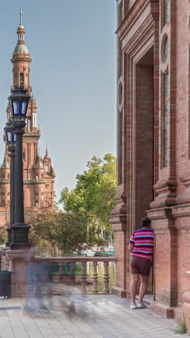 Plaza de Espana in Seville timelapse hyperlapse, tower of grand architectural complex in Maria Luisa Park built for the Ibero-American Exposition. Trees, canal and vintage streetlights under blue sky.