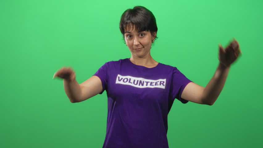 Woman in volunteer shirt raises open hands apart in studio green screen, palms visible and expressive, short hair; bemused empathy.
