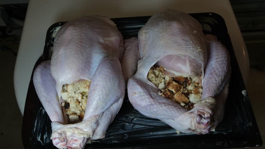 Applying melted butter to two whole stuffed turkeys on roasting pan before roasting for Christmas or Thanksgiving traditional dinner