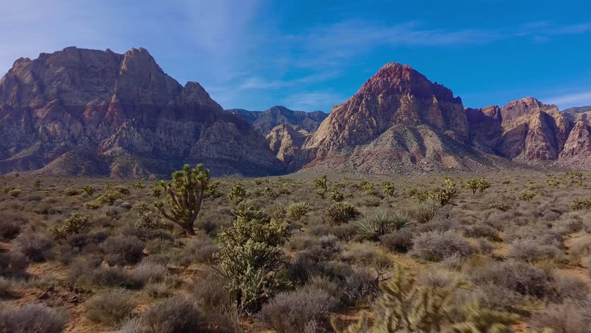 Drone flyover of a red rock canyon during the afternoon, featuring warm daylight illuminating rugged sandstone canyon walls and desert terrain.