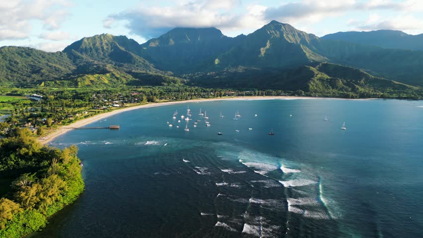 4K aerial drone view of Hanalei Bay in Kauai Hawaii, a famous surf spot and scenic tropical bay surrounded by emerald mountains and turquoise ocean water. Peaceful coastal scenery with natural light and a cinematic island atmosphere.