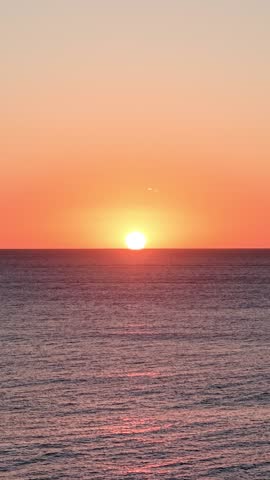 Brilliant orange sun slowly disappearing over the tranquil ocean horizon. Golden hour light reflecting on the calm sea at avellanas beach