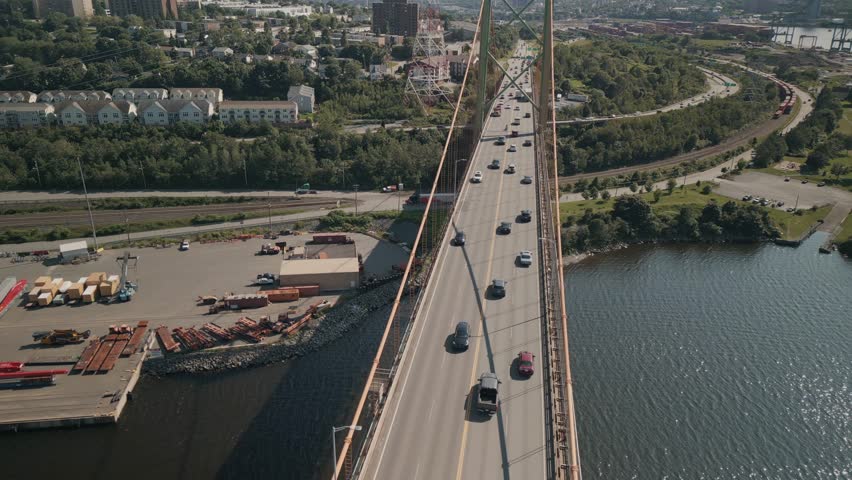 Aerial Footage Shows The Mackay Bridge In Nova Scotia Canada Stretching Across Water Between Halifax And Dartmouth On A Bright Summer Day With Clear Skies And Smooth Traffic Creating A Scenic Coastal