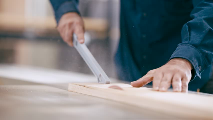 Close up of a professional woodworker's hands sawing a piece of lumber. Manual labor in a carpentry workshop creating sawdust
