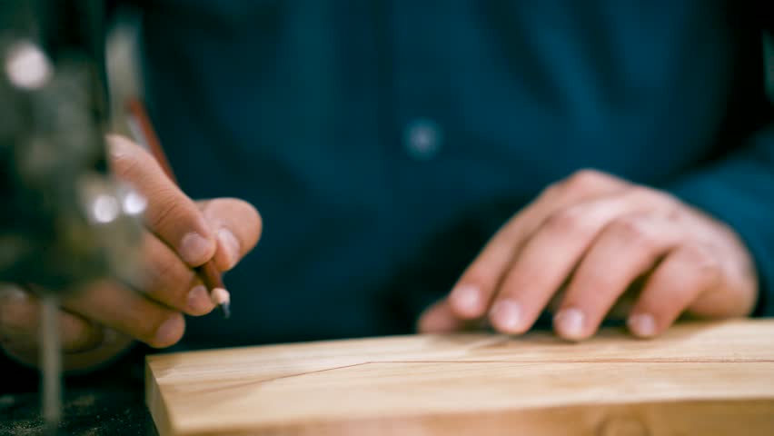 Close up of a craftsman's hands carefully tracing a cutting line with a pencil on a wooden board. Professional joinery and woodworking