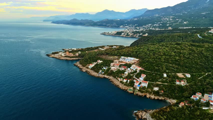 Aerial drone view of coastal buildings along the Adriatic Sea in Montenegro, with mountains in the background and scenic waters.