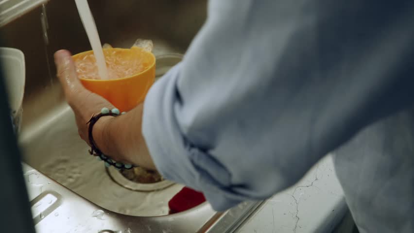 Close up of person holding bright yellow plastic dustpan with blue brush while sweeping debris. Household floor cleaning and tidying routine with cleaning tools at home.