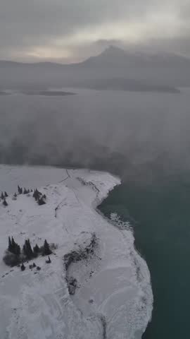 Cinematic drone panorama of fog rolling over frozen Abraham Lake and surrounding mountains in winter