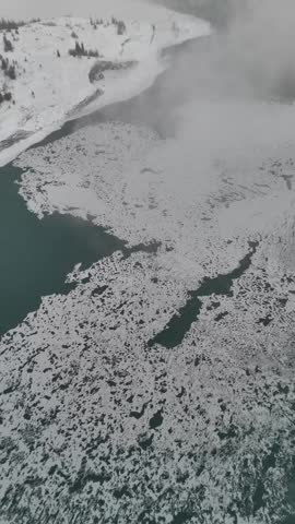 Cinematic winter drone view of Abraham Lake with ice, snow, mist, and dramatic Rocky Mountains in Alberta, Canada