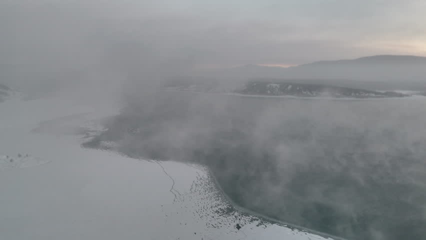 Cinematic winter drone view of Abraham Lake with ice, snow, mist, and dramatic Rocky Mountains in Alberta, Canada