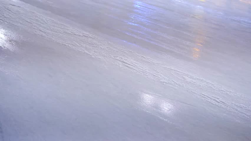 Close up view of a shimmering blue ice surface with subtle skate marks and bright light reflections