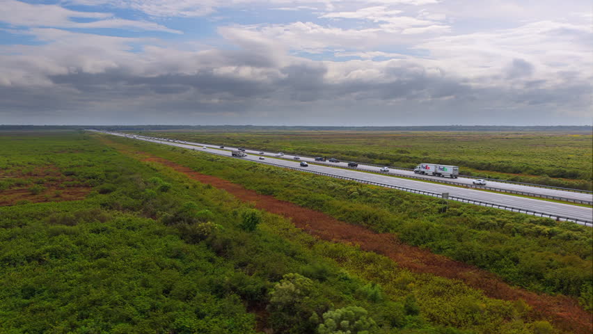 Florida freeway near Gainesville running between lush wetland areas under bright sunshine, with cars and trucks cruising along the straight road.