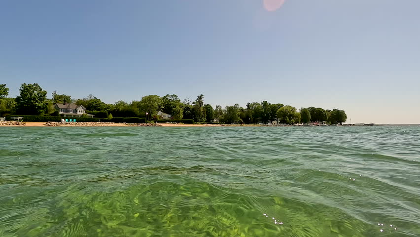 View into Land from a Beautiful Bay of Water on Lake Michigan. Surface level views of the crystal clear lake water in a bay on Lake Michigan in Northern Michigan, USA.  Boats and a beach are in the distance.