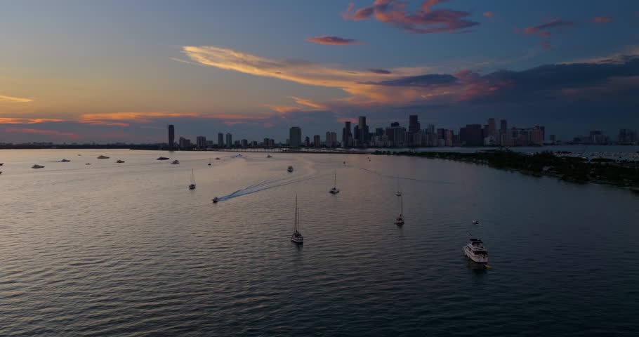 Miami city in Florida. Recreational yachts and fishing boats anchored in Biscayne Bay harbor. Evening over urban skyline with high-rise buildings in downtown.