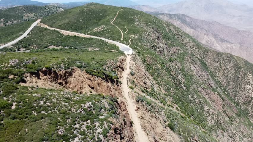 Spectacular aerial footage of Mount Laguna near Julian, Southern California. Features steep cliffs, winding roads, and hiking trails under a clear blue sky. Captures the spirit of mountain adventure. 4K