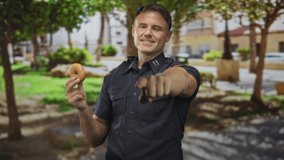 Man police officer smiling and holding donut with outstretched hand, badge visible on uniform, standing on street; playful camaraderie. - Powered by Shutterstock - Get 15% off with code: PIKWIZARD15