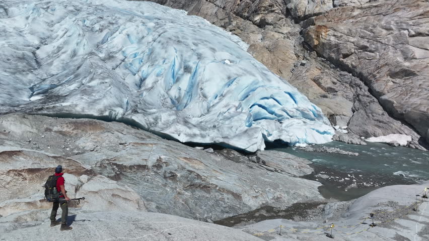 Climber examines a large norwegian glacier with blue ice in a rugged mountain setting during daylight hours.