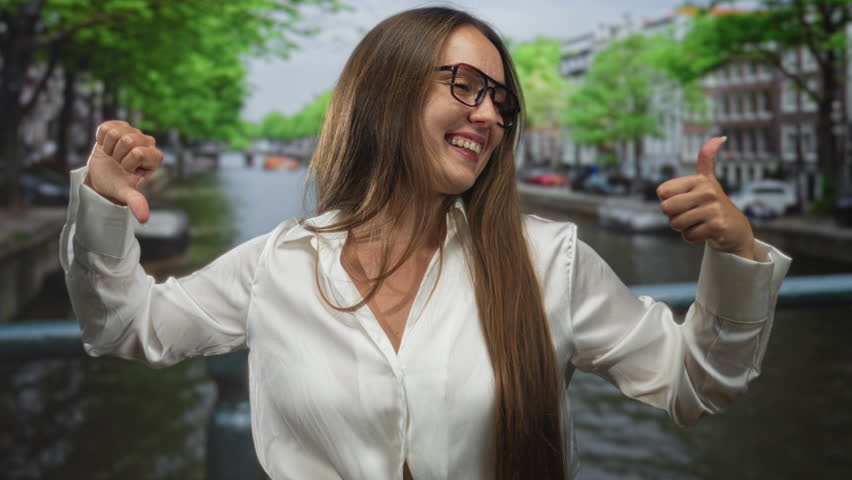 Woman thumbs up with right hand and thumbs down with left on street in amsterdam; playful contradiction.